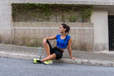 Bir şişe su, kaldırım şehir sokak üzerinde oturan kulaklıklar, müzik dinlerken egzersiz, çalıştırdıktan sonra dinlenme genç atletik erkek holding.