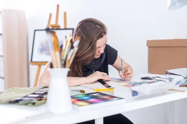 Jonge vrouwelijke artiest tekenen schets schetsboek met potlood op haar werk in de studio. Kant weergave portret van geïnspireerd schilder. — Stockfoto