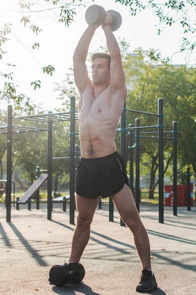 Atleta masculino muscular com braços levantados fazendo exercícios de elevação halteres . — Fotografia de Stock