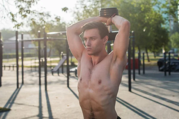 Atleta masculino muscular com braços levantados fazendo exercícios de elevação halteres . — Fotografia de Stock