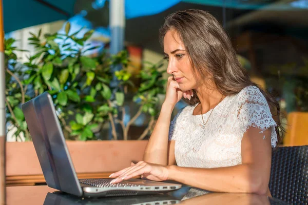 Vista lateral de la joven escritora escribiendo en su computadora portátil mientras está sentada en la cafetería del parque. Chica escribiendo netbook al aire libre . — Foto de Stock