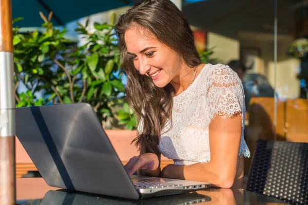 Blogger bastante sonriente usando computadora portátil para escribir blogs mientras está sentado en la cafetería al aire libre en un día soleado . —  Fotos de Stock