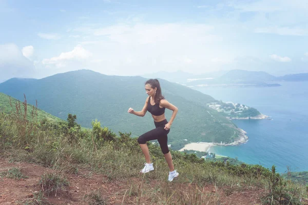 Atleta femenina Fitness vestida con ropa deportiva negra haciendo ejercicio cardiovascular, corriendo en montañas con inspiradoras vistas al mar —  Fotos de Stock