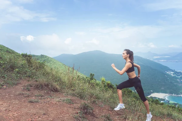 Sottile giovane atleta donna che fa esercizio cardio salendo la montagna con il mare sullo sfondo . — Foto Stock