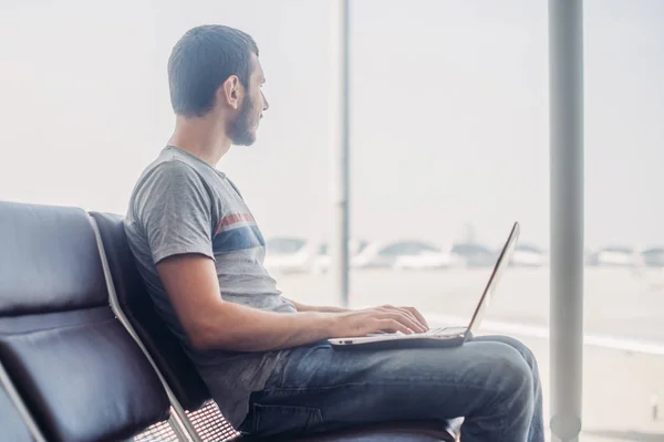 Hombre joven usando el ordenador portátil en la terminal del aeropuerto —  Fotos de Stock