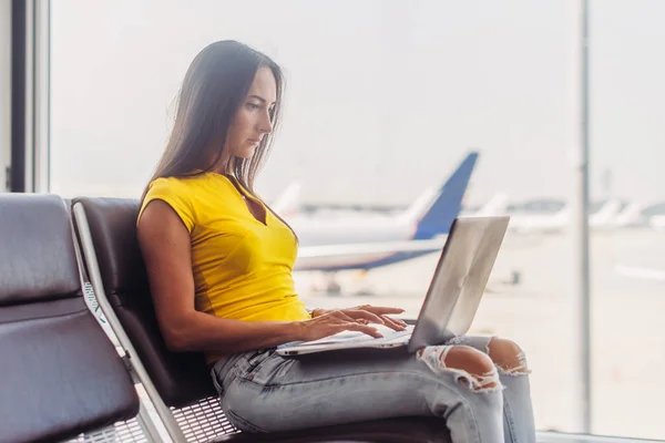Mujer joven sosteniendo un ordenador portátil en el teclado de escritura de vuelta en el interior en el aeropuerto — Foto de Stock