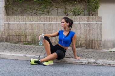 Bir şişe su, kaldırım şehir sokak üzerinde oturan kulaklıklar, müzik dinlerken egzersiz, çalıştırdıktan sonra dinlenme genç atletik erkek holding.
