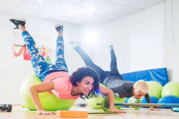 Two women exercising with stability balls doing push-ups in a gym class