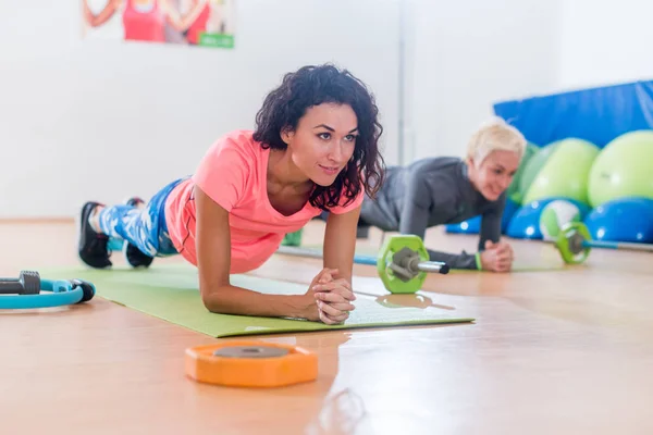 Mujeres jóvenes atractivas deportivas haciendo ejercicio de tablón de antebrazo de yoga o pose de delfín en esteras mientras entrenan en un club de fitness —  Fotos de Stock