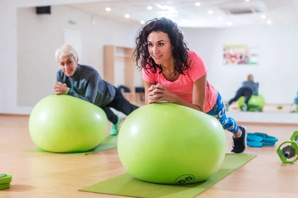 Δύο αθλητριών ευτυχισμένη άσκηση με μια ελβετική μπάλα κάνει άσκηση σανίδα στο γυμναστήριο — Φωτογραφία Αρχείου