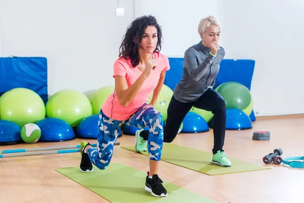 Duas mulheres caucasianas magras exercitando-se em esteiras fazendo lunges com os braços para fora na frente deles no clube de fitness — Fotografia de Stock