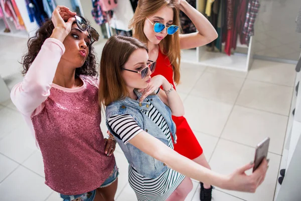 Fidanzate sorridenti che indossano occhiali da sole alla moda si divertono a scattare selfie con il telefono cellulare mentre fanno shopping nel negozio di abbigliamento — Foto Stock