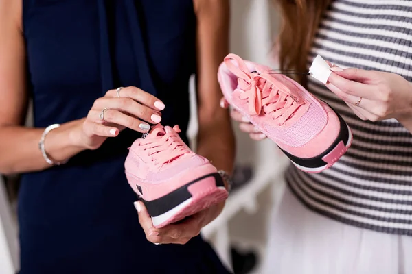 Three young girlfriends examining holding new pair of sports footwear standing in fashion showroom — Stock Photo, Image