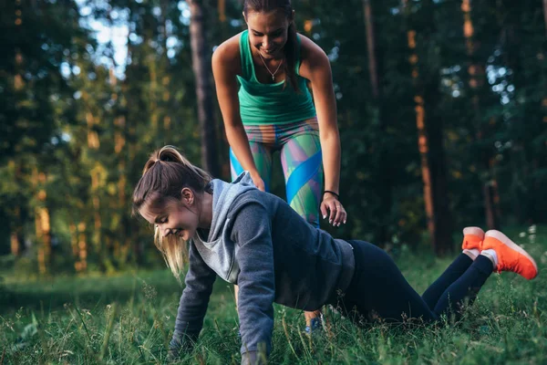 Deportiva joven entrenadora que muestra a una chica cómo hacer flexiones de rodilla mientras entrena al aire libre en verano —  Fotos de Stock