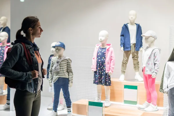 Jeune femme se tient près de la fenêtre du magasin enfants usure. — Photo