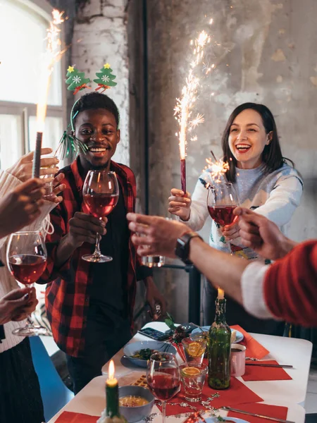 Grupo de amigos brindando bebidas en una fiesta. Personas tomando vino en el interior en unas vacaciones de invierno —  Fotos de Stock