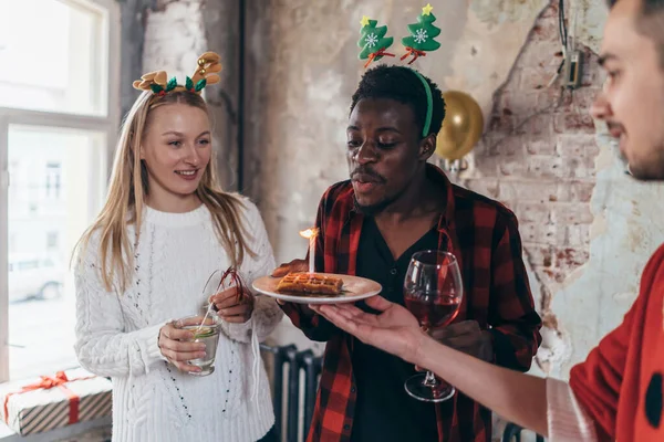 Gruppo di amici che festeggiano il compleanno con la torta. L'uomo africano spegne la candela sul waffle . — Foto Stock