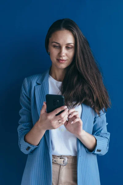 Ung kvinna som använder sin smarta telefon stående mot väggen — Stockfoto