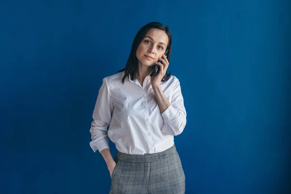 Mujer de pie cerca de la pared hablando en el teléfono móvil mirando la cámara —  Fotos de Stock