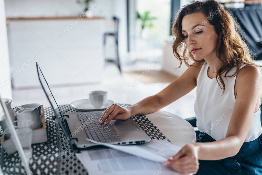 Woman using laptop while sitting at table. Young businesswoman sitting in kitchen and working on laptop.