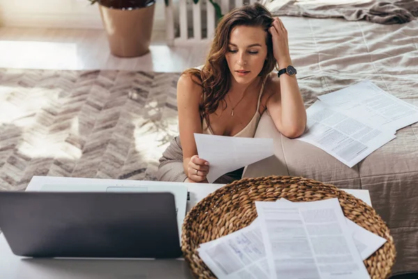 Ung kvinna håller en bit papper och läser, hon arbetar hemma. — Stockfoto