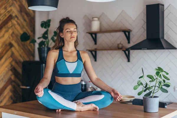 Sportieve vrouw zit op een tafel met haar ogen dicht en mediteert — Stockfoto