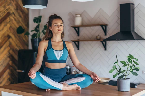 Sportliche Frau sitzt mit geschlossenen Augen auf einem Tisch und meditiert — Stockfoto