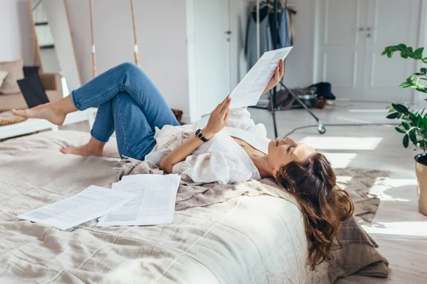 Una joven está acostada en una cama en el dormitorio leyendo — Foto de Stock