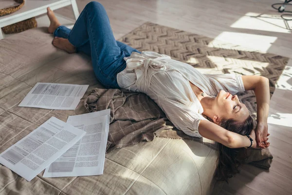 Μια νεαρή γυναίκα στο σπίτι είναι ξαπλωμένη ανάμεσα στις εφημερίδες στο κρεβάτι και ξεκουράζεται — Φωτογραφία Αρχείου