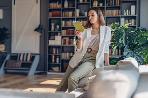 Femme assise sur le canapé le matin, lisant le livre à la maison — Photo