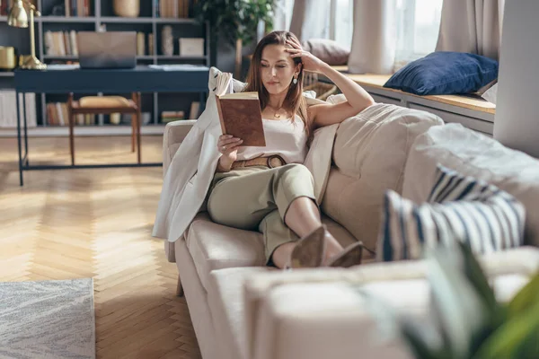 Nő fekszik a kanapén és könyvet olvas otthon — Stock Fotó