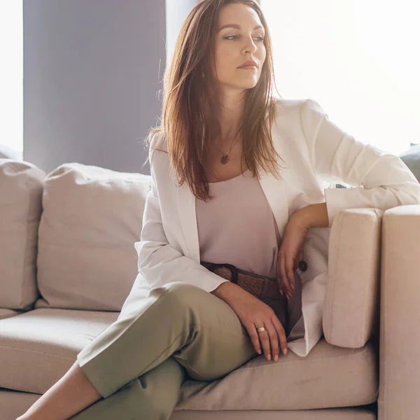 Porträt einer jungen Frau in lässiger Businesskleidung, die auf der Couch sitzt. — Stockfoto