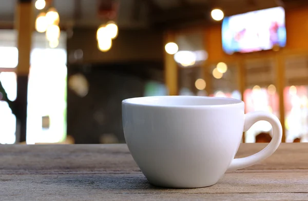 Taza de café blanco en la mesa de madera en la cafetería fondo borroso . — Foto de Stock