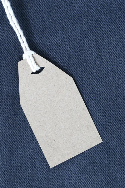 Etiqueta de papel marrón con cuerda de cáñamo atada en mezclilla o jeans . — Foto de Stock