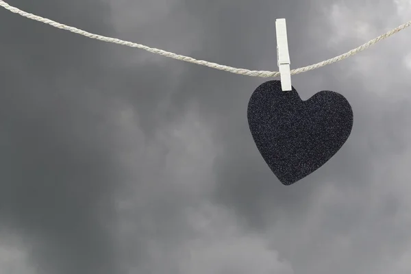 Corazón negro papel colgando de una cuerda de cáñamo marrón en las nubes de lluvia ba —  Fotos de Stock