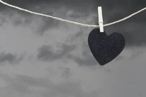 Schwarzes Herzpapier hängt an einem braunen Hanfseil auf Regenwolken. — Stockfoto