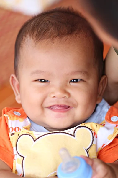 Asiatisches Baby lächelt glücklich und hat eine Flasche Milch in der Hand. — Stockfoto