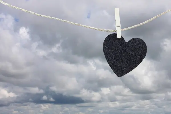 Corazón negro papel colgando de una cuerda de cáñamo marrón en las nubes de lluvia ba —  Fotos de Stock