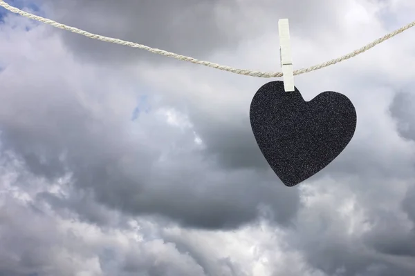 Papel preto coração pendurado em uma corda de cânhamo marrom em nuvens de chuva ba — Fotografia de Stock