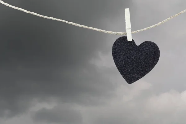Corazón negro papel colgando de una cuerda de cáñamo marrón en las nubes de lluvia ba —  Fotos de Stock