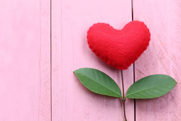 Красное сердце помещается на розовый деревянный стол в связи с ветками о — стоковое фото