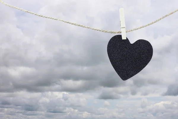 Papel preto coração pendurado em uma corda de cânhamo marrom em nuvens de chuva ba — Fotografia de Stock
