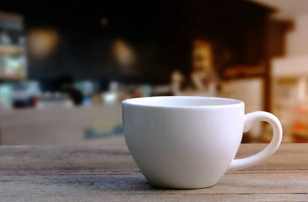 Taza de café blanco en la mesa de madera en la cafetería fondo borroso . — Foto de Stock