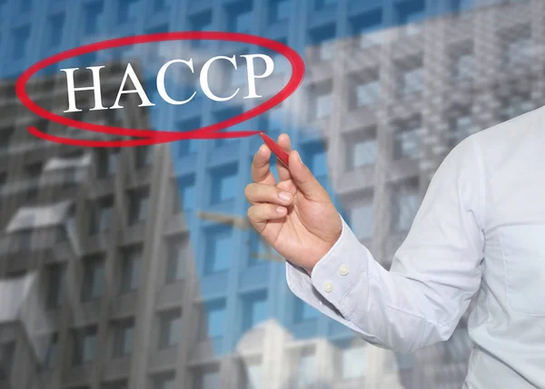 Mano di giovane uomo d'affari scrivere la parola HACCP su grattacieli ba — Foto Stock