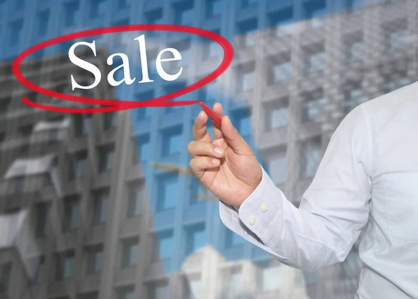 Hand eines jungen Geschäftsmannes schreibt das Wort Verkauf auf Wolkenkratzer bac — Stockfoto