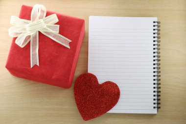 Boş kitap ve ahşap zemin üzerinde kırmızı hediye kutusu.