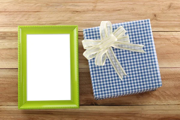 Blauer Geschenkkarton in der Nähe eines grünen Holzrahmens auf dem Holzboden. — Stockfoto