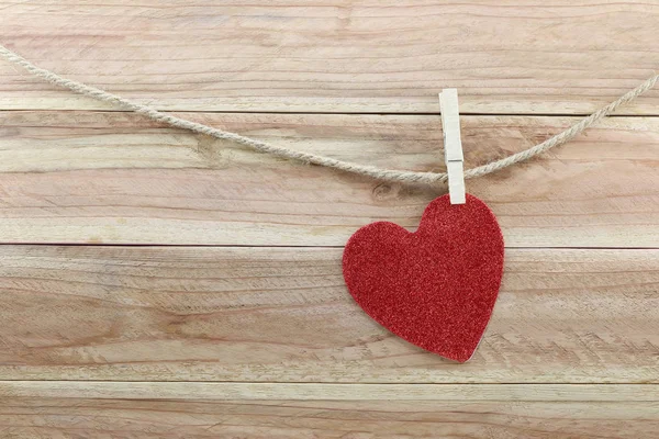 Forma de corazón rojo colgando de una cuerda de cáñamo sobre fondo de madera marrón . — Foto de Stock