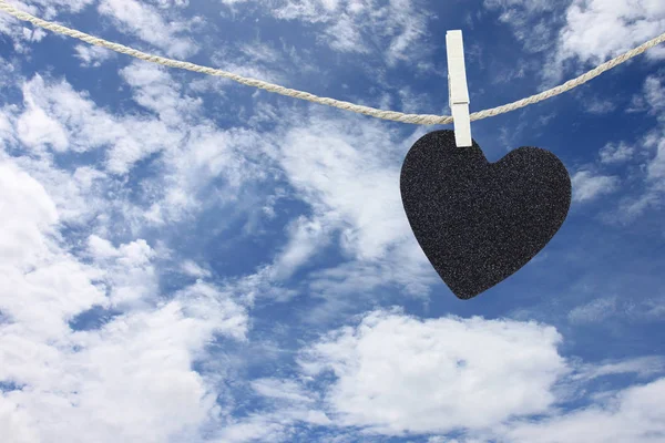 Coração preto pendurado na corda de cânhamo no fundo do céu azul . — Fotografia de Stock