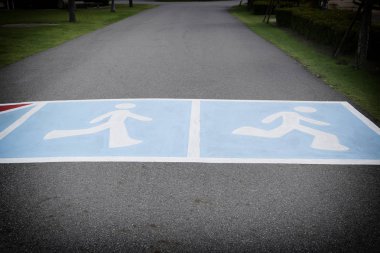 parkta yol asfalt ve insanları yürüyüş ve r sembolü var.